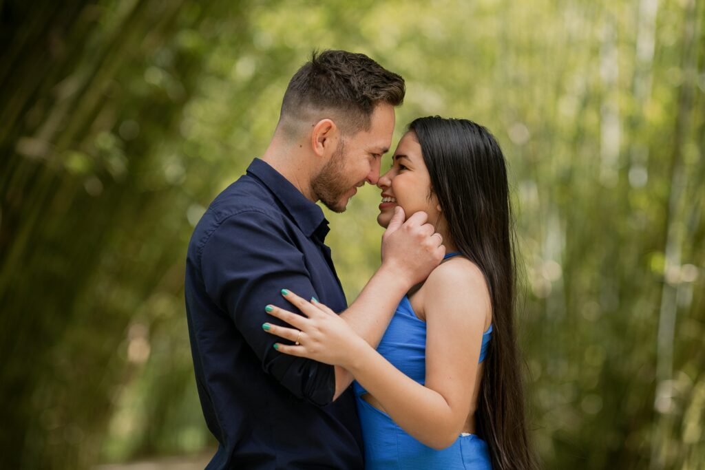 Interracial couple smiling and embracing in a lush green outdoor setting.