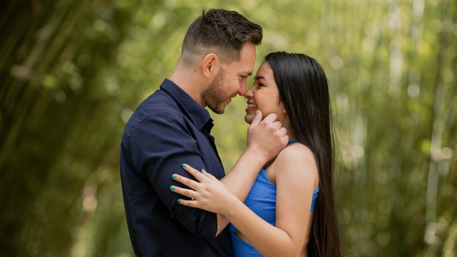 Interracial couple smiling and embracing in a lush green outdoor setting.