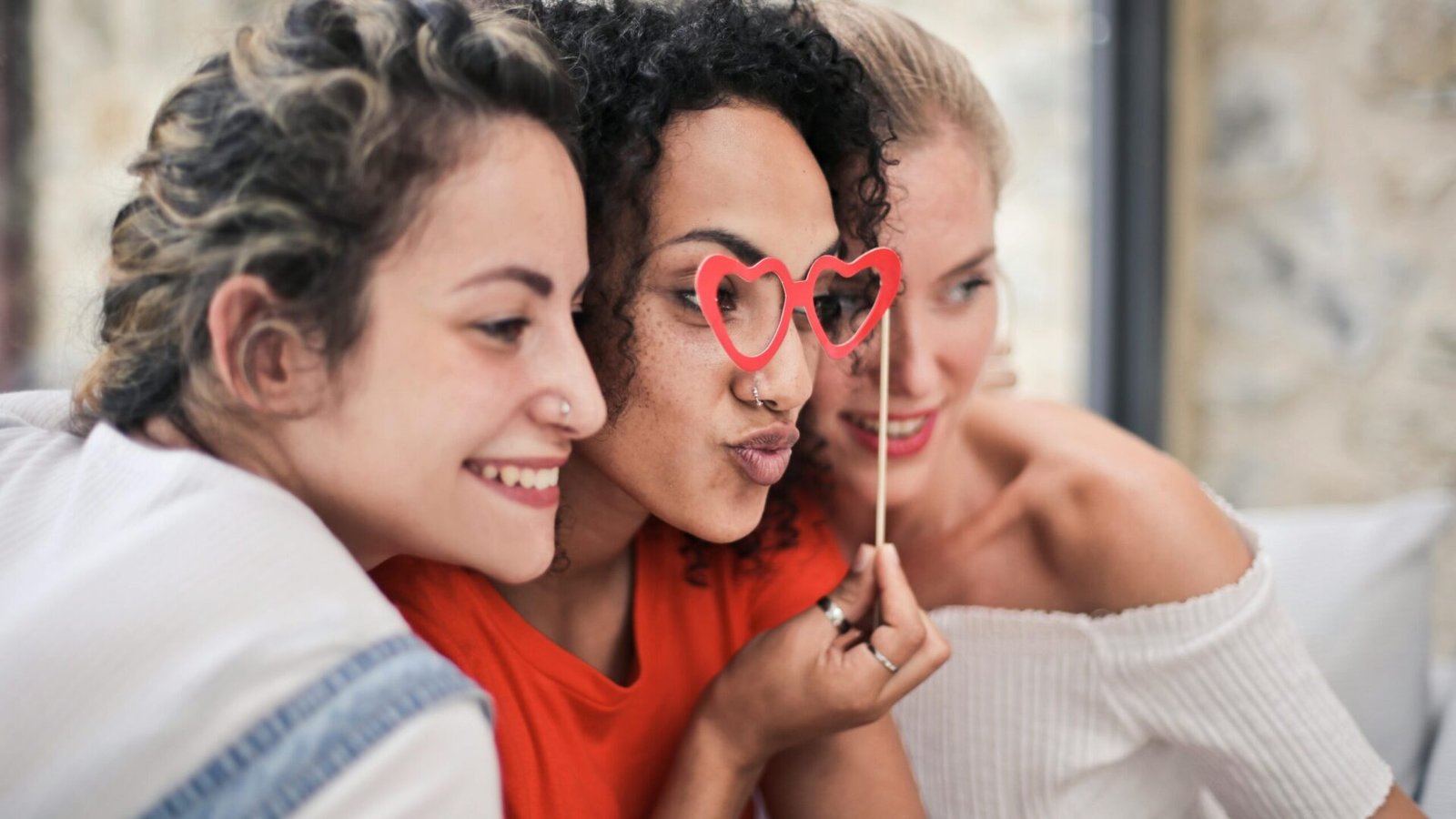 Three women enjoying a playful moment with heart-shaped glasses, symbolizing friendship and fun.