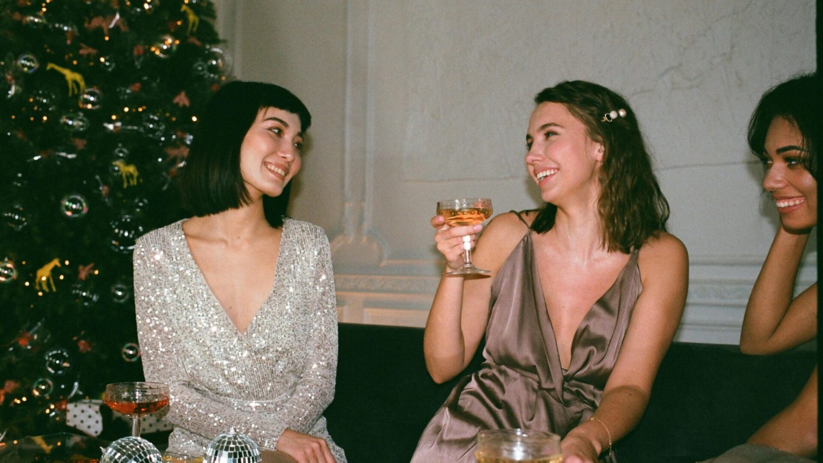 Three women enjoying festive celebration indoors with cocktails and joy.